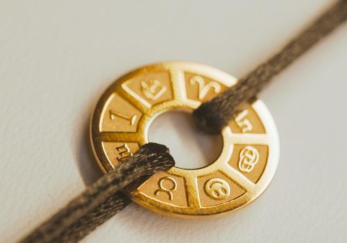 Gold personalized jewel medallion engraved with zodiac signs, tied on a black cord bracelet